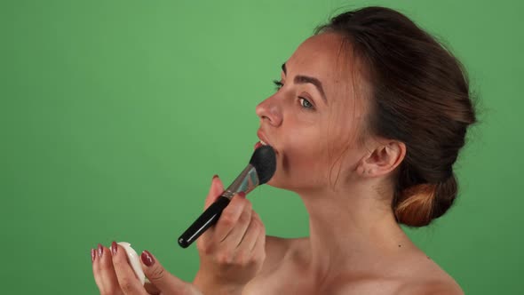 Gorgeous Young Woman Applying Makeup on Green Background