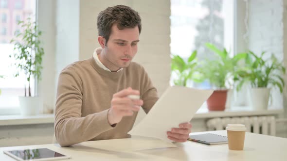 Man Celebrating Success While Reading Documents in Office