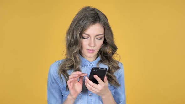 Young Girl Excited for Success While Using Smartphone Isolated on Yellow Background