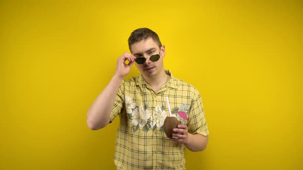 A Man in Sunglasses and a Hawaiian Shirt Takes Off His Glasses and Holds a Coconut Pina Colada in