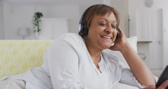 Happy african american senior woman wearing headphone enjoying using smartphone and smiling