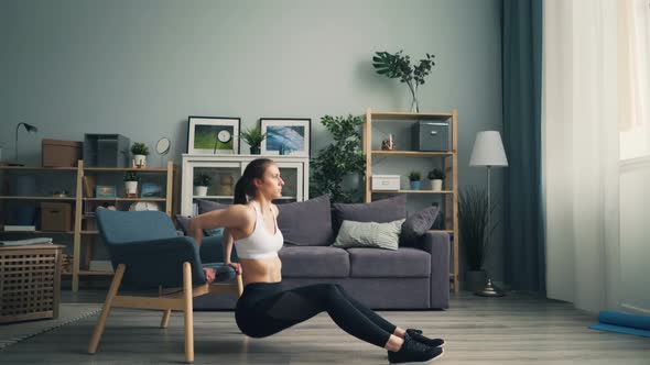 Fit Young Woman Doing Pushup Dips Holding Armchair Working Out in Apartment