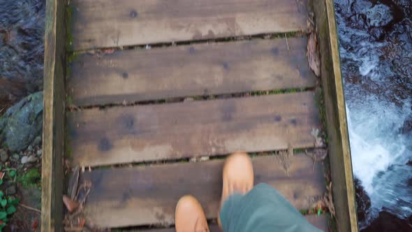 Close-up of legs of male traveler walking across a bridge to mountain river.