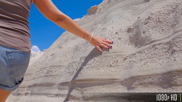 Closeup of woman hand touching white sandy texture rock wall formation at Sarakiniko, Greece