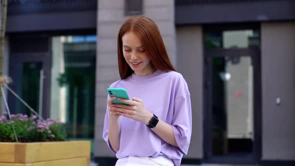 Joyful Redhead Lady Wearing Casual Fashion Clothing Reading Message on Mobile Phone