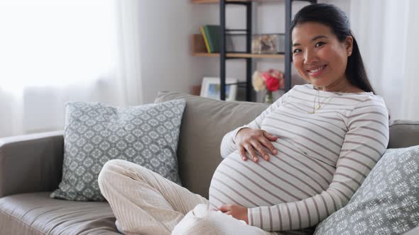 Happy Pregnant Asian Woman Sitting on Sofa at Home