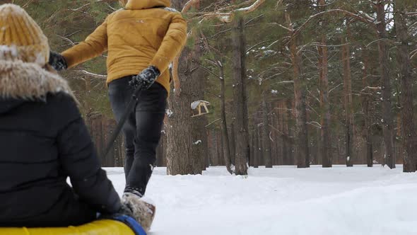 Man Is Sliding Woman on Tubing in Winter Park in Slow Motion Back View