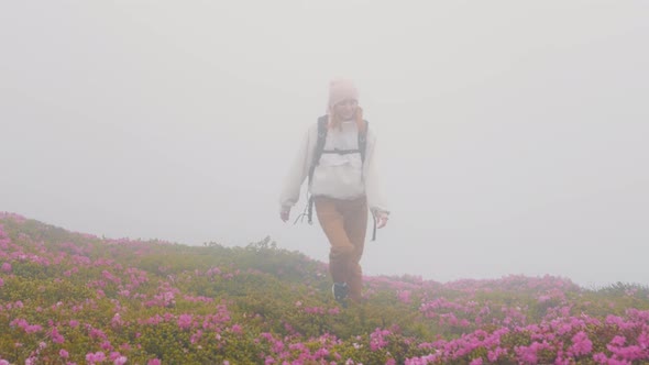 Woman with a backpack walks along a mountain road in rainy weather.