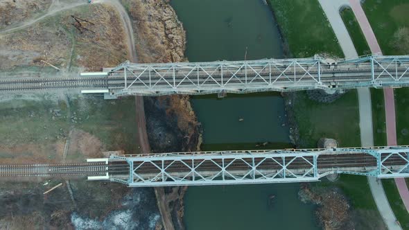 Metal railway train track bridge across river, aerial top view.