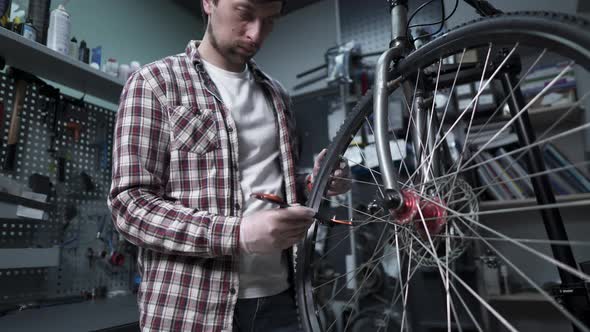 A Male Bicycle Mechanic Aligns the Tension Spokes of a Bicycle Wheel with a Special Tool at the