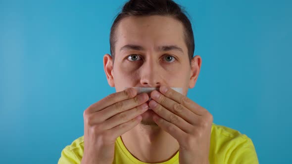 A Young Millennial Guy is Taping His Mouth Shut