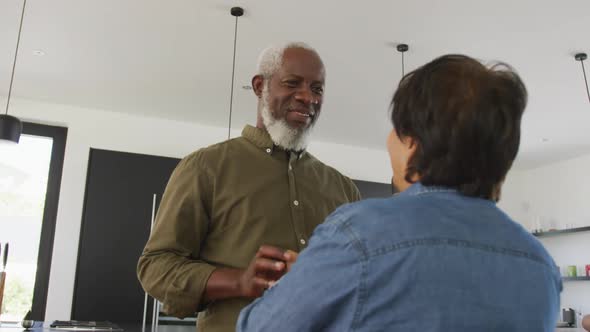 Happy senior diverse couple dancing in kitchen at retirement home