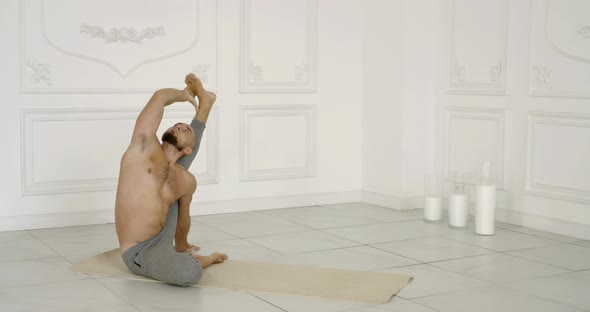 Flexible and Plastic Male Yogi with a Beard Doing Yoga on a Rug in a Bright Studio. He Does