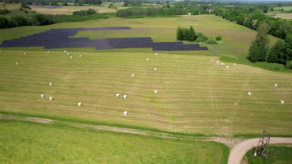 Ascending aerial shot of agricultural fields with hay bale beside solar panels farm - 4K shot