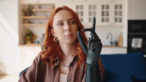 Young Redhaired Woman Looks at Her Bionic Prosthetic Left Hand and Alternately Flexes and Unbends