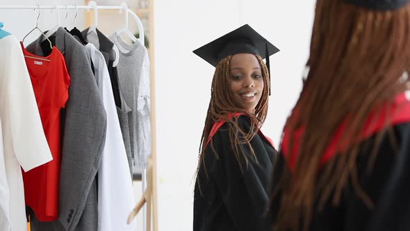 African Woman Trying on Fitting Cap and Gown and Looking in Mirror with Happy Smile Spbi