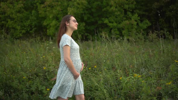 Happy Young Pregnant Woman Walks in Nature and Strokes Her Belly