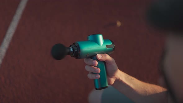 Athletic Male Massages Muscles with Hand Massage Gun Recovering From Stadium Running Workout