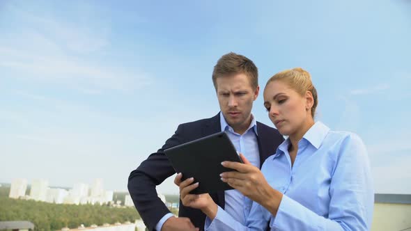 Male and Female Employees Scrolling Tablet App Outdoors Preparing Presentation