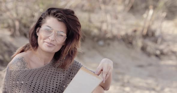 Beautiful woman reading on a beach notices the camera then smiles and laughs