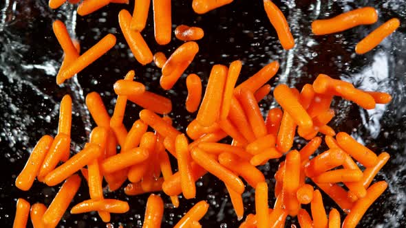 Super Slow Motion Shot of Flying Fresh Baby Carrots and Water Side Splash on Black at 1000 Fps