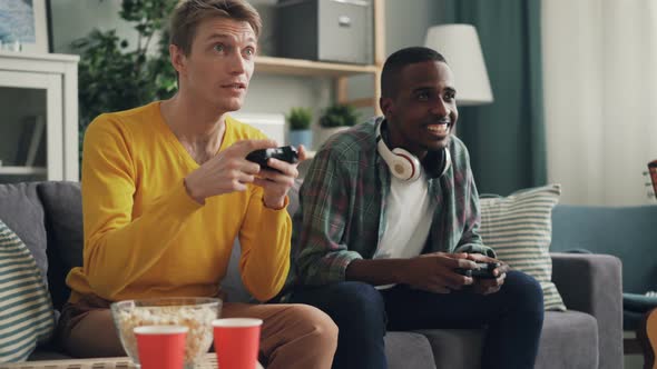 Male Friends Are Enjoying Video Game Playing Together at Home Holding Joysticks