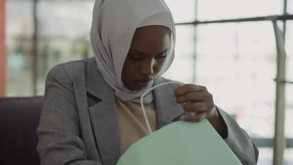 Black Lady with Hijab Looks Inside Shopping Bag in Mall