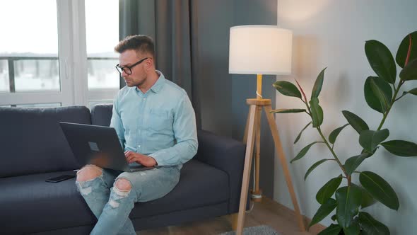 Man with Glasses Sitting on the Sofa with Laptop and Working in Cozy Room