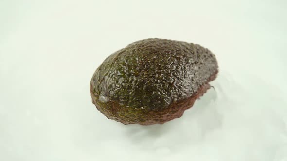 Rotating ripe avocado in water on a white background. Slow motion.