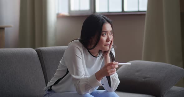 Young Sad Nervous Woman Holding a Pregnancy Test with Two Stripes