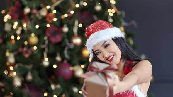 Portrait of Happy Asian Woman Wearing Santa Claus Hat and Suit Smiling and Gives Present in Gift Box