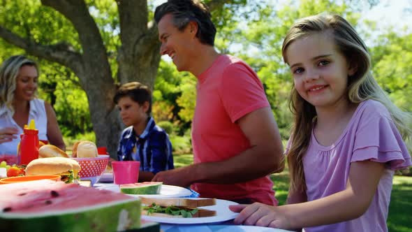 Girl sitting at the table and having meal with her family in park 4k