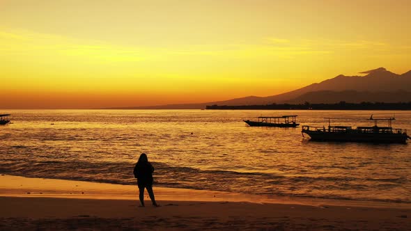 Silhouette of woman greets people in the anchored boats on calm lagoon reflecting orange sky after b