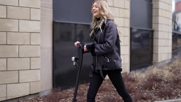 Cheerful Blond Female Walking with Scooter