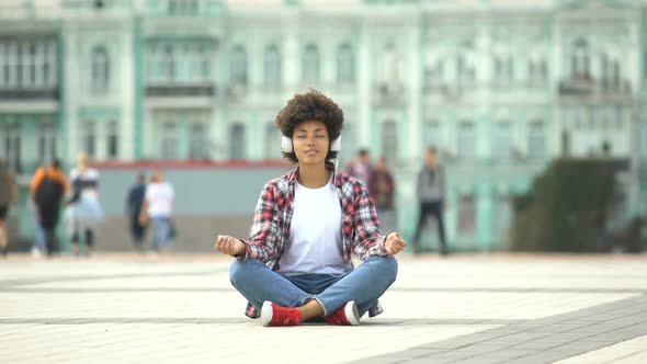 Carefree Young Female Sitting in Lotus Pose and Listening to Music in Headphones