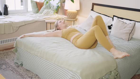 Young Woman in Sports Outfit Does Yoga Stretching on Bed