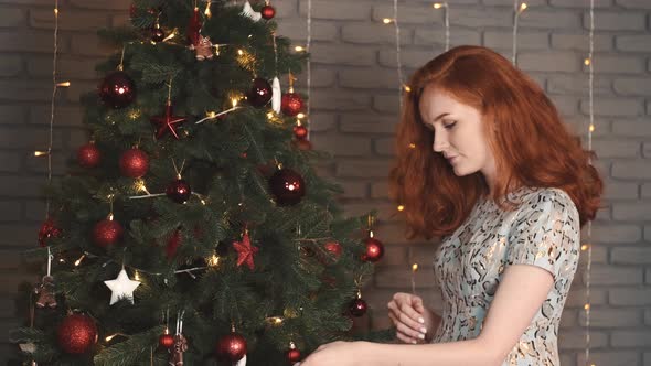 Pretty Young Lady in Elegant Dress Decoraing Xmas Tree for New Year's Party