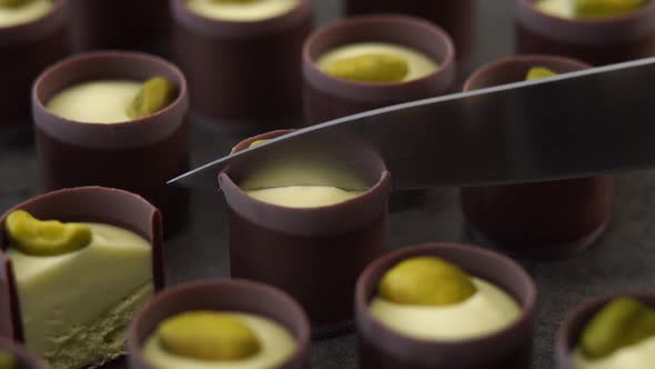 Close Up of Knife Cuts Milk Chocolate Candie with Creamy Filling and Pistachio Nuts