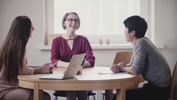 Two Beautiful Positive Caucasian Girls Talk To Japanese Man at a Job Interview By the Table