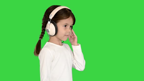 Cute Girl Dressed in White Holding Headphones with One Hand and Nodding Her Head To the Music While