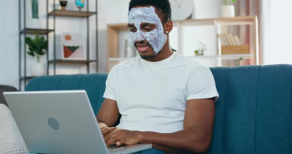 Black-Skinned Guy with Face Mask Sitting in front of Laptop and Chatting with Friends