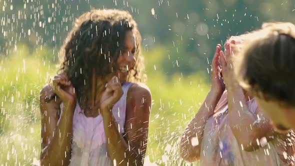 Friends Splashing Water on Two Excited Young Women Covered in Color Powder