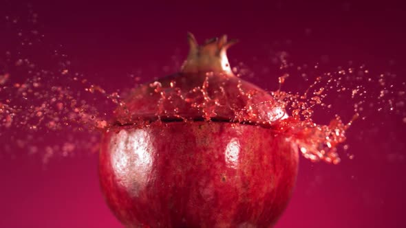 Half Pomegranate Falling and Splashing on Fuchsia Background