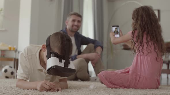 The Boy and Girl Laying on the Floor on Fluffy Carpet, the Brother Using Virtual Reality Glasses