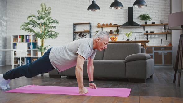 Senior Man is Doing Pushups Exercise on Pink Mat at Home Taking Care of His Health