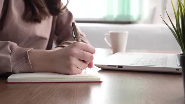 A Girl Takes Notes in a Notebook From Her Laptop