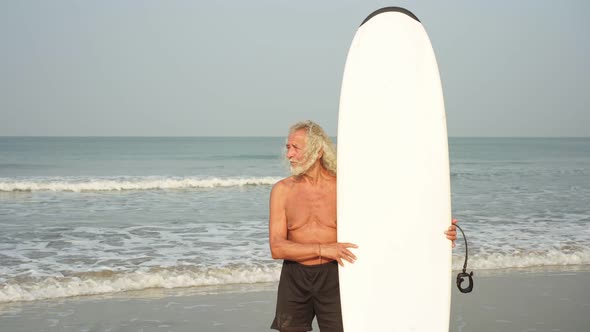 Portrait of an Old Healthy Man with a Surfboard on the Background of the Sea. Athletic Old Man. 