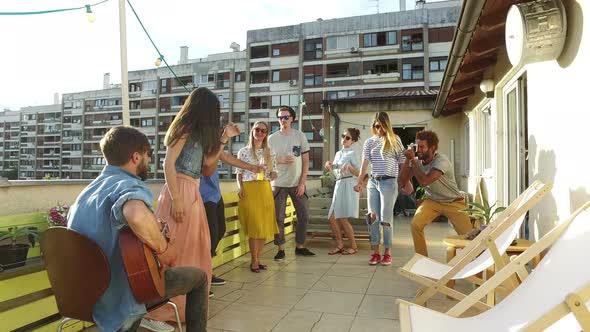 Happy people dancing and playing guitar at the rooftop party on sunny day