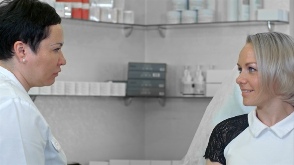 Cosmetologist talking with female client in bathrobe sitting