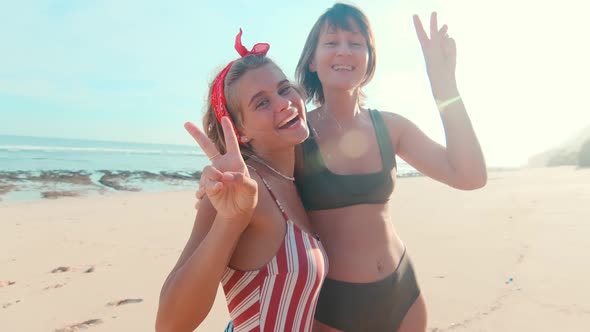 Young Caucasian Women Smiling Showing Gesture of Victory Stands on Sea Beach